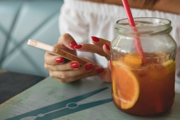 真っ赤なネイルをした女性がカフェで携帯をいじっている写真