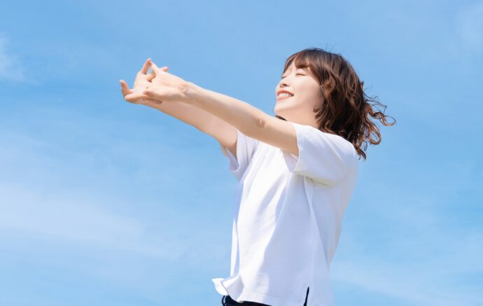 青空の下で伸びをするポジティブな女性