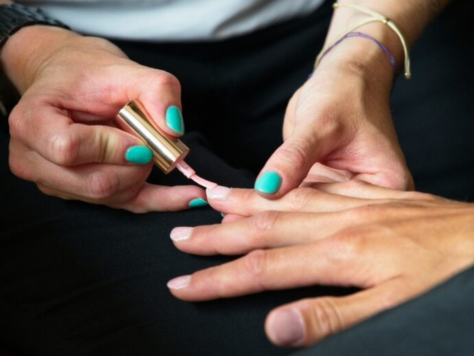 ヌーディーなピンクのネイルカラーを塗っている手元のアップ