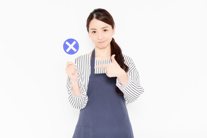 バツのパネルを持つエプロン姿の女性