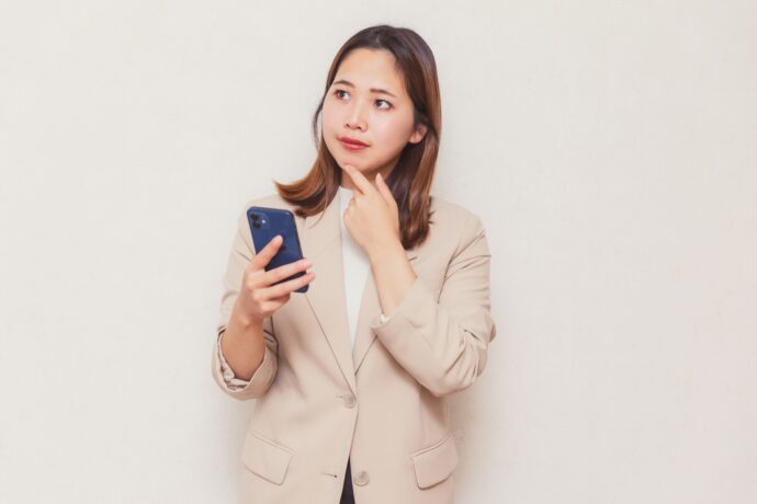 スマホ片手に悩むベージュスーツの女性