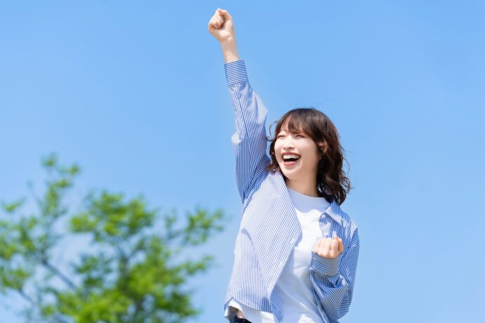 青空の下でガッツポーズをする女性