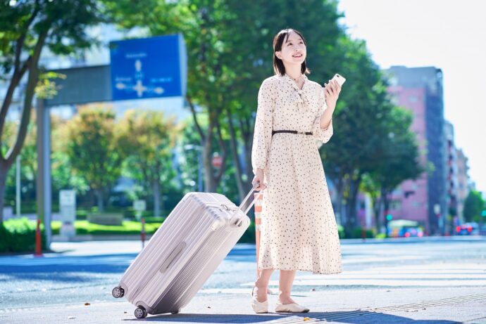 スーツケースとスマホを持って歩く若い女性の画像