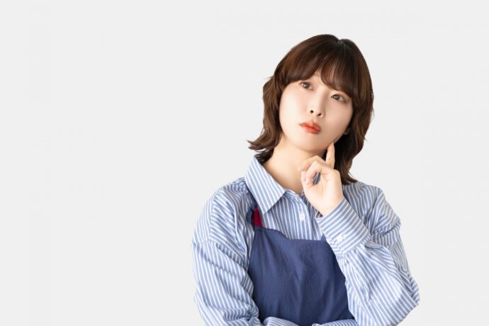 考えごとをするエプロン姿の女性の画像