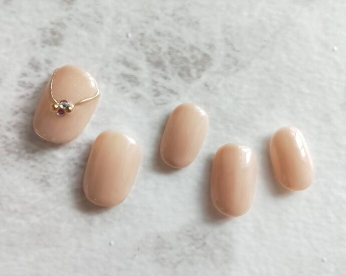 一部にアクセサリーネイルをしたベージュのワンカラーオフィスネイル