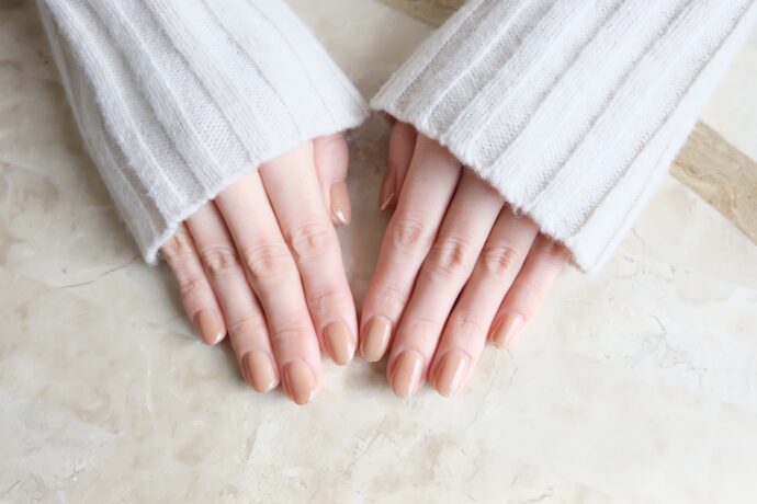 白いニットにヌーディーネイルをした女性の手