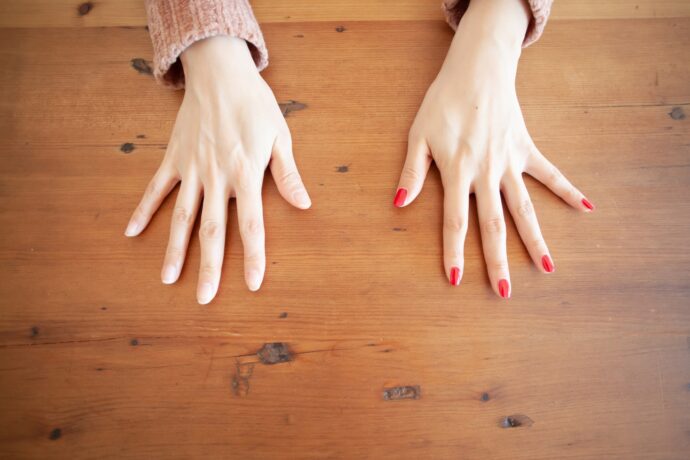 片方の手に赤マニキュアを塗った手元
