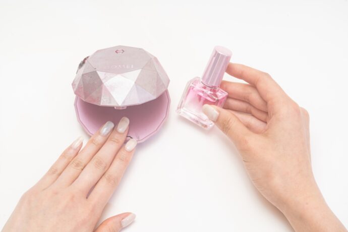 コンパクトなネイルライトとネイルオイルを持つ手元