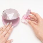 コンパクトなネイルライトとネイルオイルを持つ手元