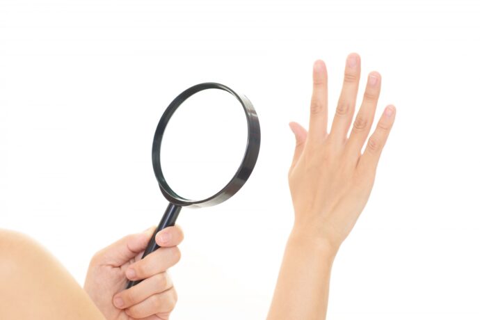 虫眼鏡で自分の手を見る女性