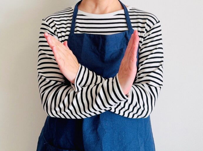 手でバツマークを作るエプロンの女性